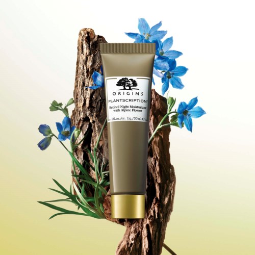 En tub med Origins hudvård med blå blommor och trä, reklam för en nattcreme med alpin blomma.