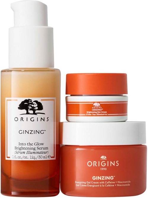 Three skincare products with orange, white, and transparent bottles and jars, labeled 'Origins Ginzine' and 'Into the Glow' serum.