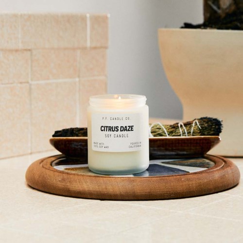 Een witte kaars met 'Citrus Daze' op een houten dienblad met andere kaarsen en decoraties op de achtergrond.