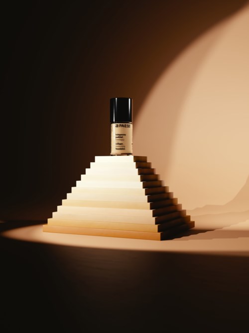 En makeuppflaska på en pyramidtrappa med ljus och mörk bakgrund. Flaskan är centrerad och belyses.