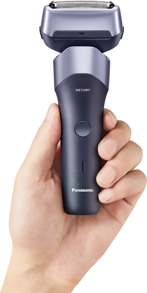 Een hand houdt een grijze en zwarte elektrische scheerapparaat met een grote scheerkop. De scheerapparaat heeft een aan/uit-knop en merknaam Panasonic.