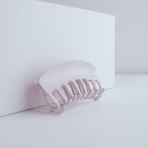 A white ceramic hair clip attached to a white wall with soft shadows and minimal background.