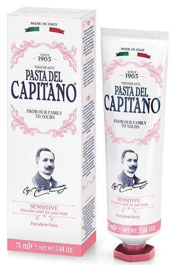 En tandkrämstub och box med varumärket 'Pasta del Capitano,' tillverkad i Italien, med en mans ansikte, rosa dekorativa detaljer och känslig, parabensfri påstående.