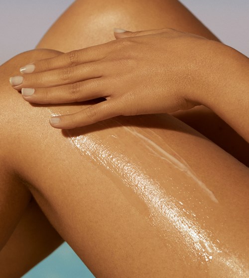 En person applicerar lotion eller olja på sin lår, med skinande, slät hud och välskötta naglar.