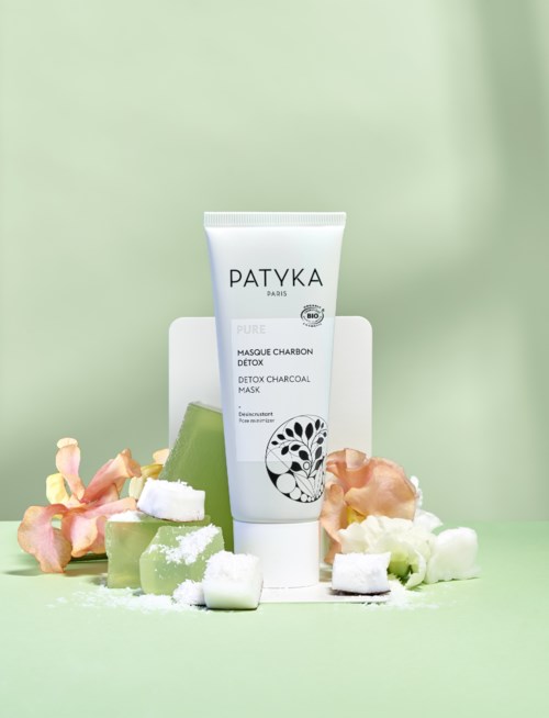 En tub med Patykas detoxkol förpackning omgiven av tvål och blomblad på ljusgrön bakgrund.