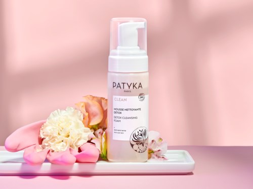 En rosa och vit flaska av Patyka detoxrensskum med blommor på ett fat.