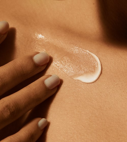 En persons hand sprider vit lotion på huden, skapar en glänsande fläck på en slät yta.