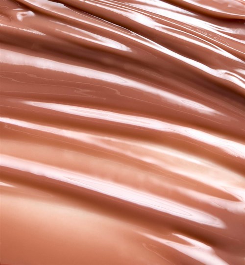 Lähikuva vaaleanpunaisesta-beigeistä kermamaisesta tekstuurista, mahdollisesti meikkituote kuten meikkipohja tai lotion.