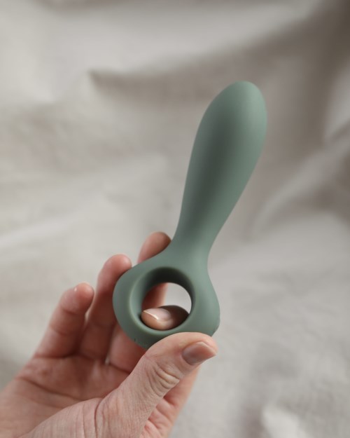 Een groen siliconen apparaat met een lus en een lange handgreep, vastgehouden in iemands hand.