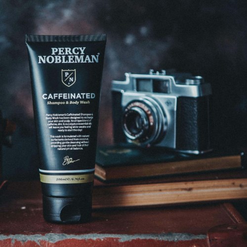 Ein schwarzer Tuben von Percy Nobleman Caffeinated Shampoo und Body Wash steht auf einer Holzoberfläche neben einer Kamera.