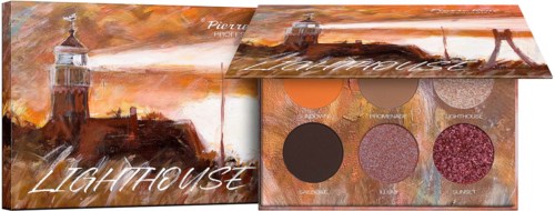 A makeup palette with four eyeshadows in front of a painting of a lighthouse at sunset.