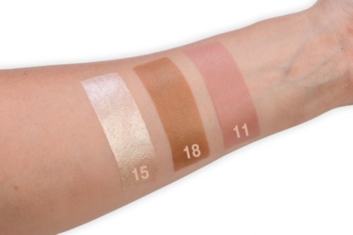 Swatches of makeup or foundation shades numbered 15, 18, and 11 on a person's arm.