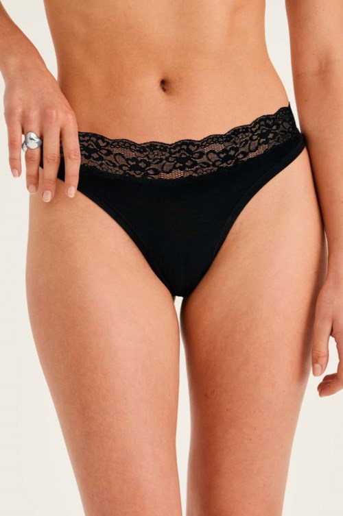 Zwarte kanten ondergoed bij een vrouw met een hand die een ring laat zien, neutrale achtergrond.