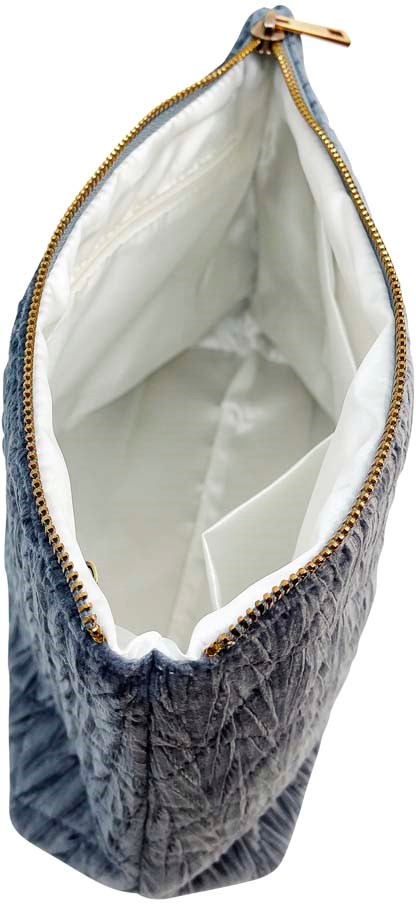 A velvet bag with a gold zipper, white interior, and small pocket inside. It is seen from above.