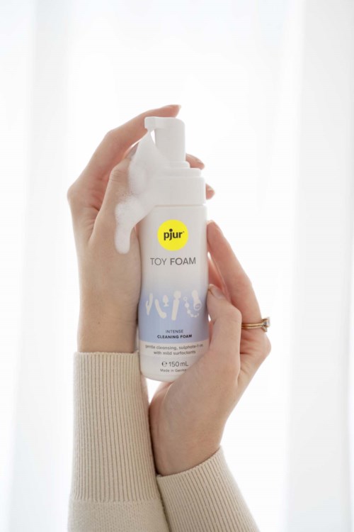 Eine Person hält eine weiße Flasche mit Pjur Toy Foam Reinigungsschaum, mit Schaum, der aus der Oberseite läuft.