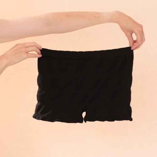 En person håller i ett par svarta shorts mot en ljus bakgrund.