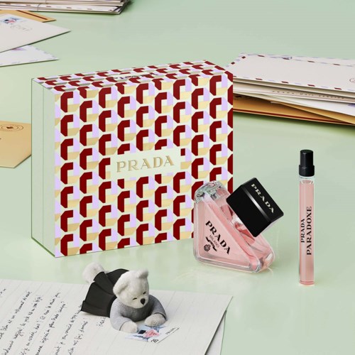 Prada gavepakke med parfume, lip gloss og en bamse på en grøn overflade.