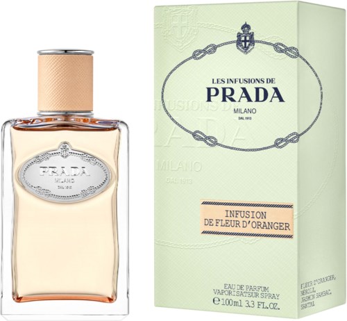 A perfume bottle and box with light green color, blue logo, and text indicating Prada and orange blossom scent.