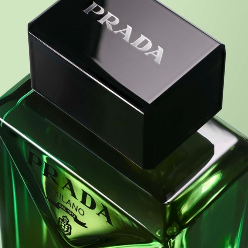 Een groene Prada-parfomfles met zwarte dop en zilveren logo, glanzend oppervlak, op een groene achtergrond.
