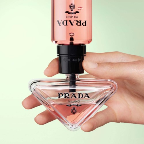 En hand håller en Prada parfymflaska med rosa topp och klar triangelformad glasbas.