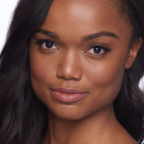 A close-up of a smiling woman with dark hair and smooth skin, looking directly at the camera.