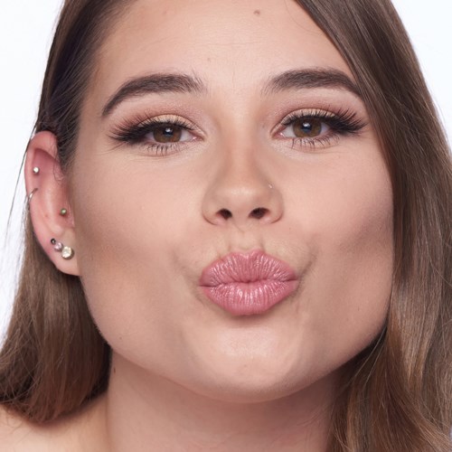 A woman with brown hair, makeup, and piercings, makes a puckering face, lips protruding.
