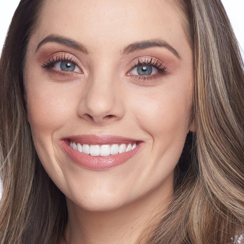 A woman with long brown hair, bright blue eyes, and a big smile showing her teeth.