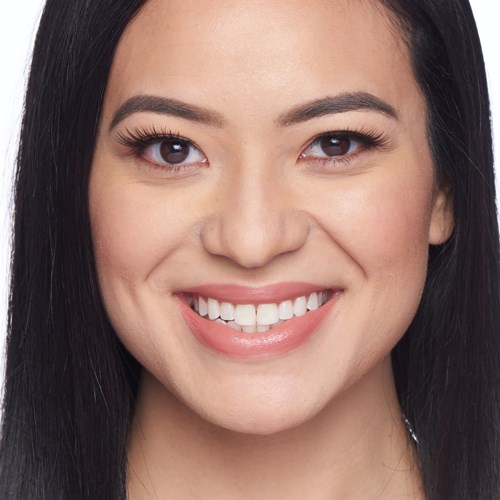 A young woman with long black hair smiling, showing white teeth and clear skin.