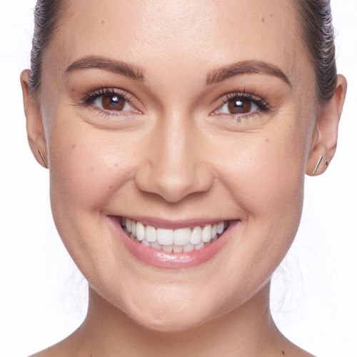 A close-up of a woman with a bright smile, clear skin, brown eyes, and earrings, looking directly at the camera.