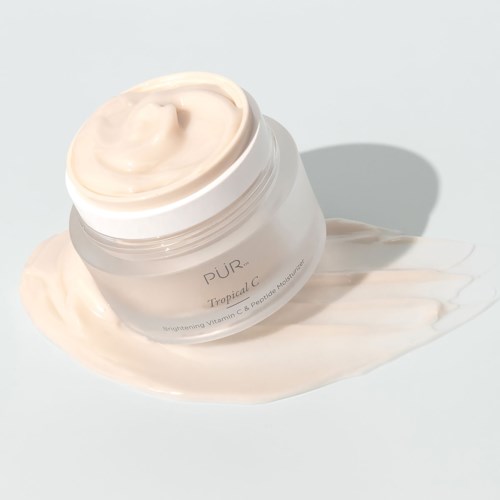 A jar of cream with a small dollop on top, spilled slightly on a light background. The jar has text on it.