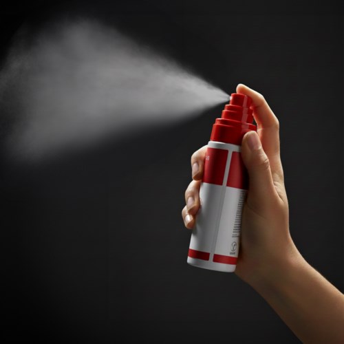 Eine Hand sprüht weißen Dampf aus einer roten und weißen Aerosoldose gegen einen schwarzen Hintergrund.