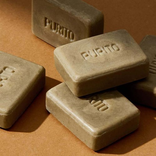Saippuapala, jossa on 'PURO' kaiverrettu, aseteltu ruskealle taustalle.