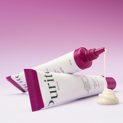 Two tubes of nourishing cream with purple caps, one open with cream spilling out, set against a pink background.