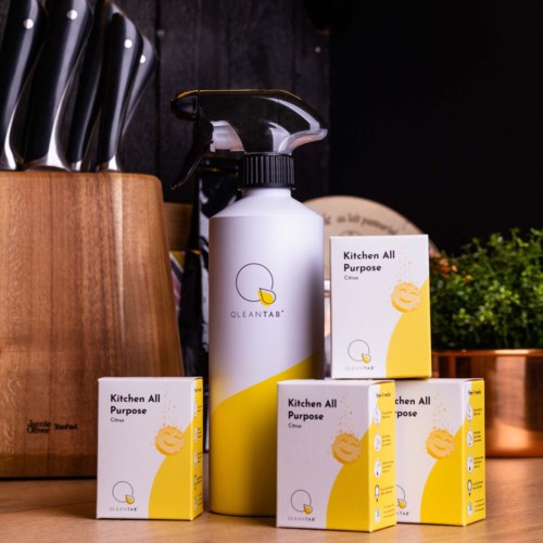En sprayflaska med rengöringsprodukt omgiven av fyra liknande produkter på en köksbänk.