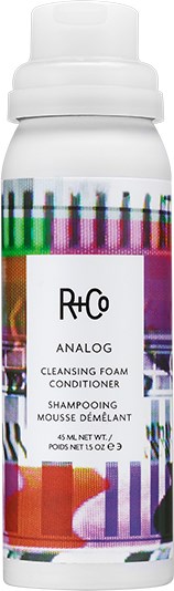Een witte fles met kleurrijke lijnen en vormen, gelabeld als Rh+Co Analog reinigingsschuimbalsam.
