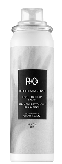 En vit flaska med en svart etikett som säger R+Co och Bright Shadows Root Touch-Up Spray, avsedd för hårfärgning.