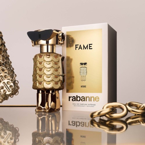 Een parfumfles met goud en glitterdesign, naast een doos met 'FAME' door Rabanne, en gouden kettingen.