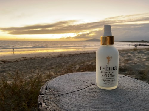 En vit flaska med Rahua förtrollad regnskogslotion på ett träytor vid stranden vid solnedgången.