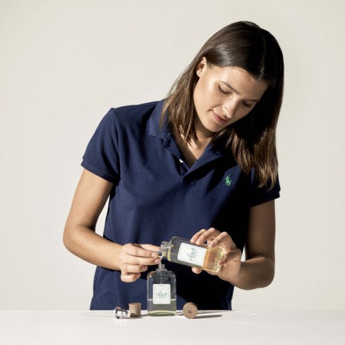 A woman in a navy blue polo shirt pouring liquid into a bottle, with other bottles and coins on the table.