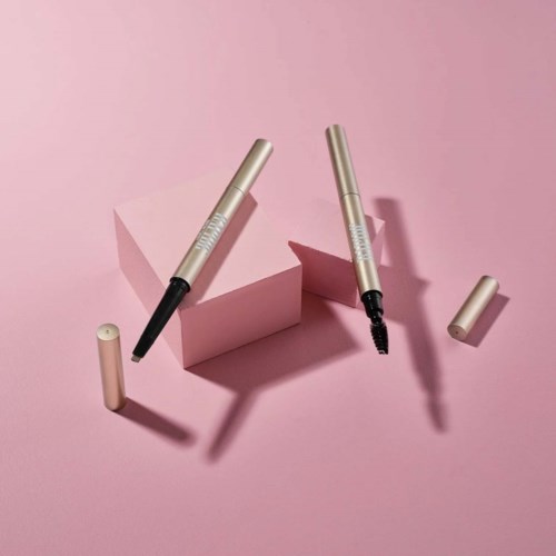 Dwa eyelinery, jeden otwarty z pędzelkiem, na różowym tle z geometrycznymi kształtami.
