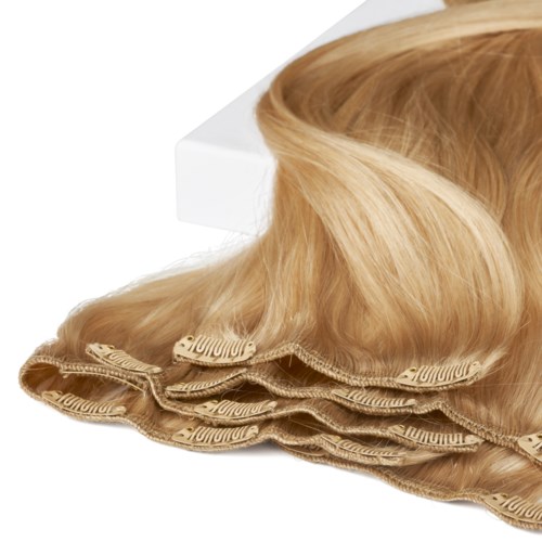 Blonda hårförlängningar eller peruk placerade på en vit bakgrund, med några delar som visar en klämma eller bandfäste.