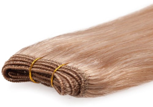 En bunt med lyseblond hårforlengelser sikret med gullbånd, ligger på en overflate.