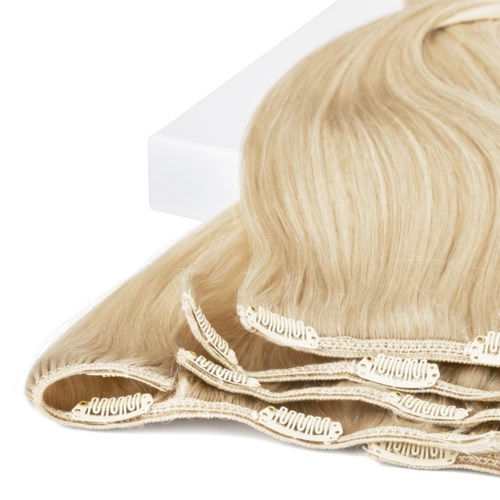 A blonde wig on a white surface, with a band or ribbon at the base.