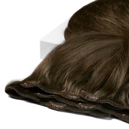 A brown wig with a lace front, placed on a white surface, with the hair slightly curled and shiny.