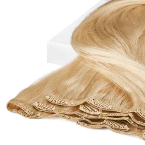 A blonde hairpiece with several layers of hair extensions on a white surface.