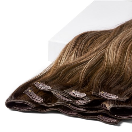 A stack of brown hair extension weaves with clips on top of a white surface.