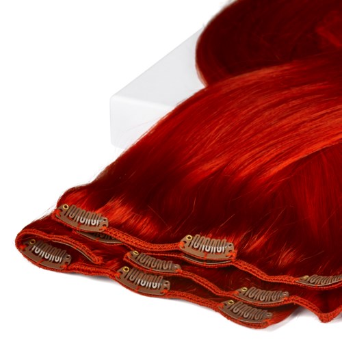 Red hair extensions with hair clips lie on a white surface.