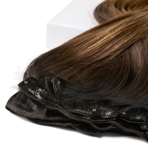 A wig with brown hair and a black lace front, displayed on a white surface.