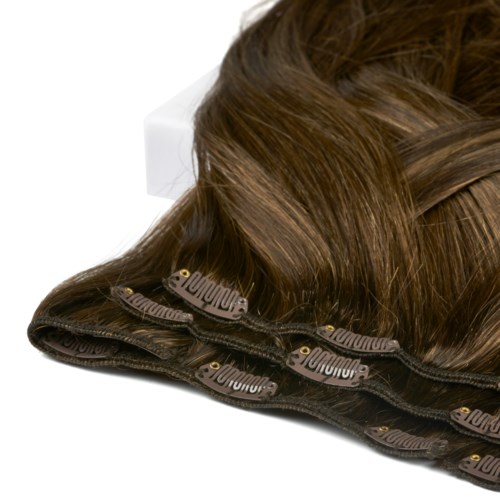 A bundle of brown hair extensions with a black zipper attached, lying on a white surface.