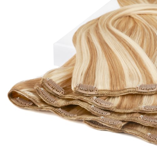A blonde lace front wig with multiple wefts, partly curled, on a white surface.
